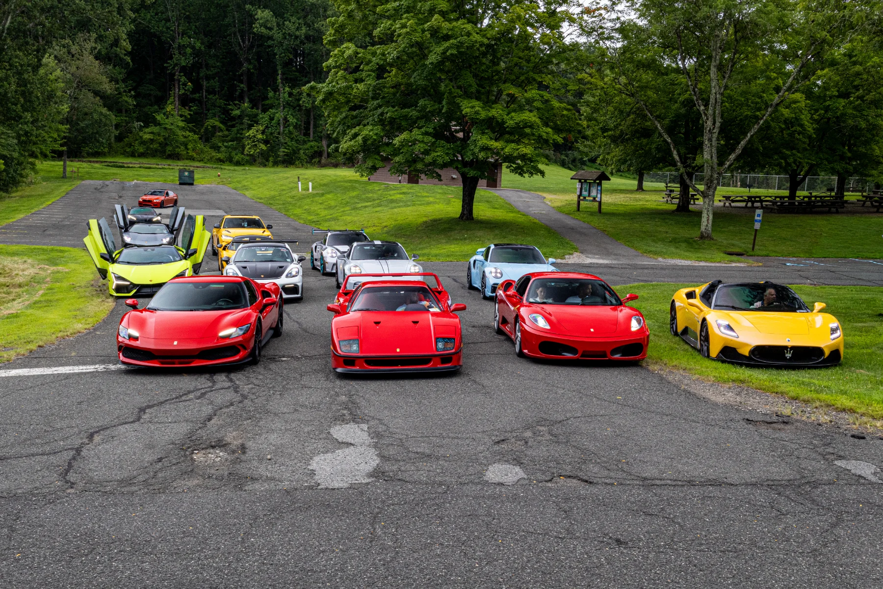 Red and yellow sports cars lined up beside a tree-lined park.