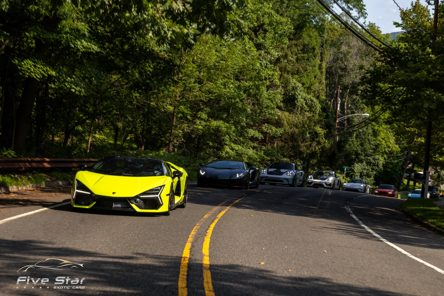 A yellow sports car leading a group along a wooded road.