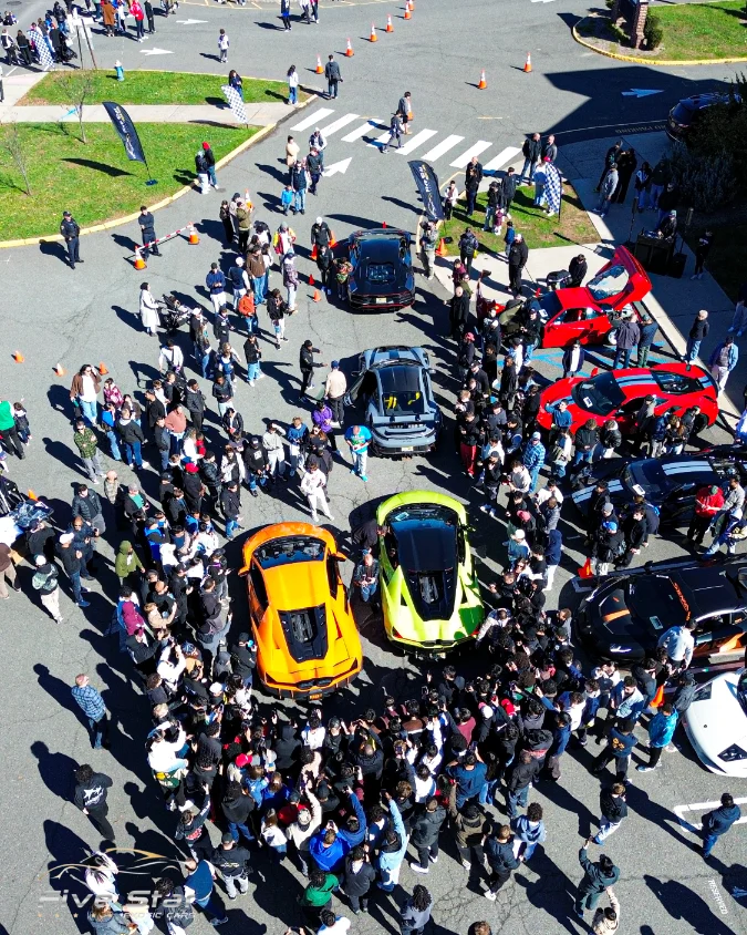 An overhead view of visitors gathered around sports cars at an outdoor car gathering.