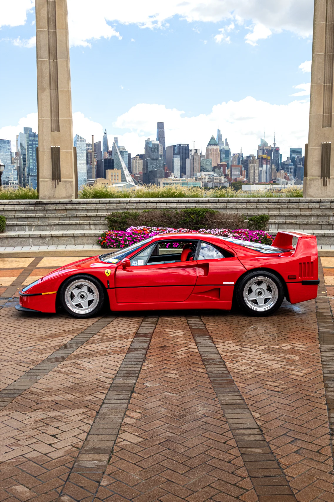 A red sports car parked between stone columns with a city skyline beyond.