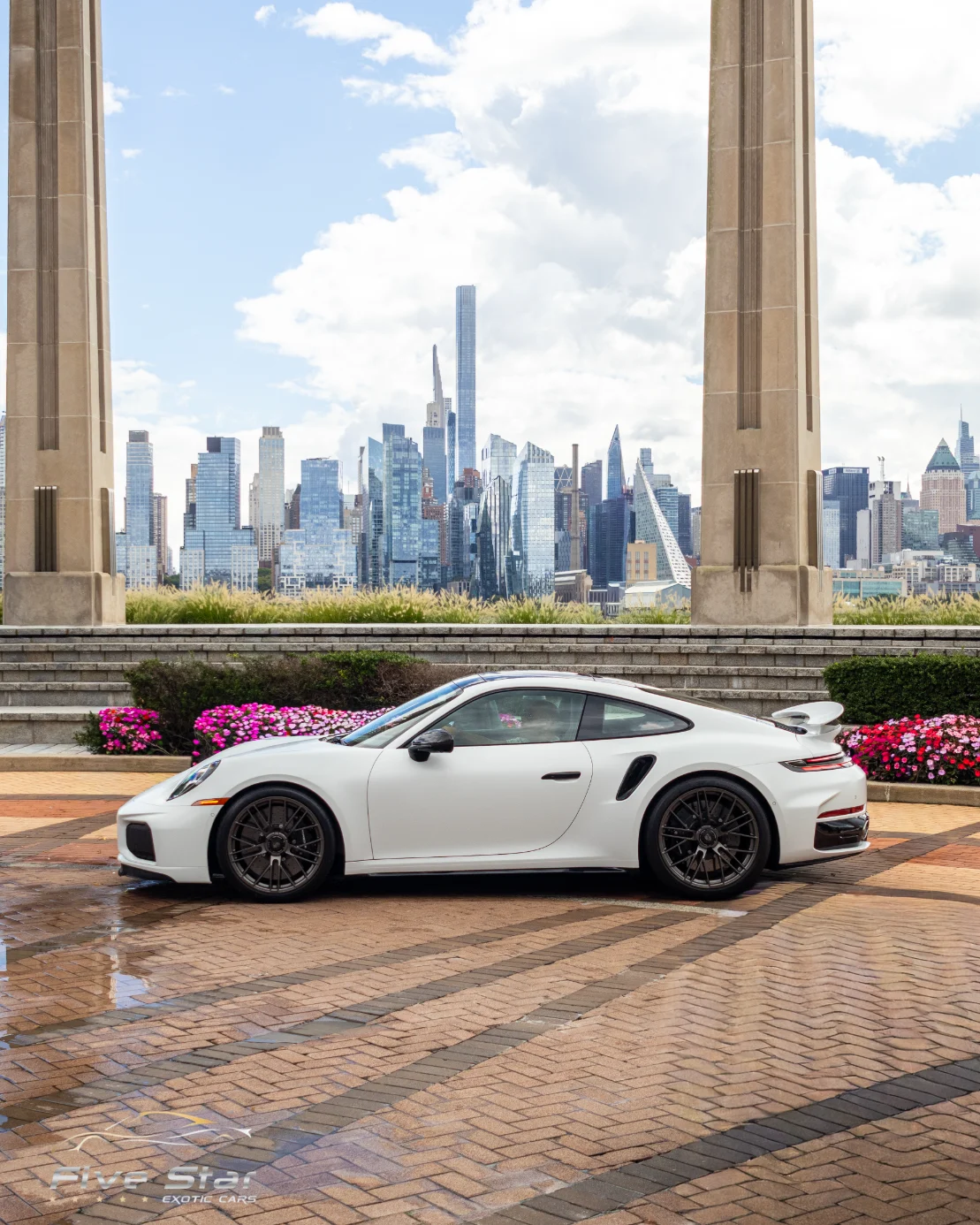 A white sports car parked on a brick terrace overlooking the city skyline.